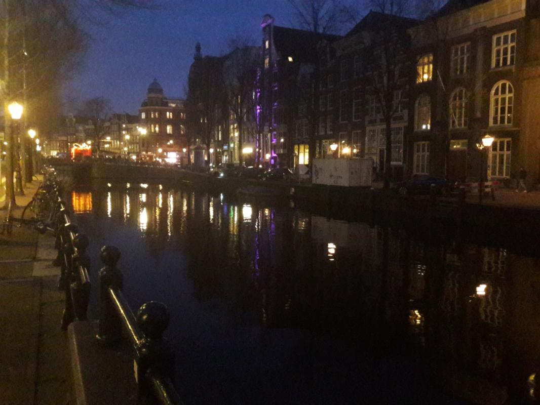 A canal in Amsterdam photographed at night. The light of the houses and street lamps reflects on the