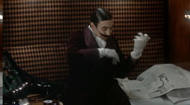 Poirot in his cabin is reading a newspaper before going sleep.